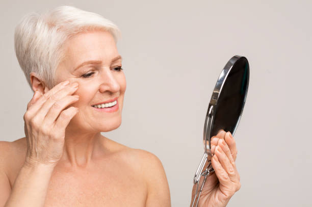 istock Beautiful elderly lady looking at mirror and applying anti-aging cream. 1174441419