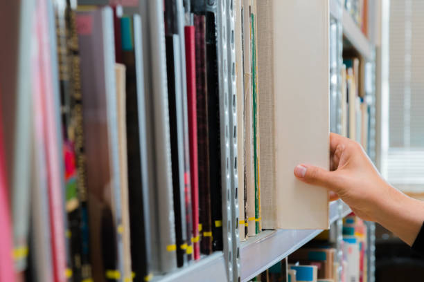 istock Young student picking a book from the shelf in the library. Preparing for exams, young man searching for or choosing a book in the public library in university 1174443560