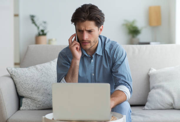istock Concerned Man Talking On Mobile Phone Sitting At Laptop Indoor 1174444404