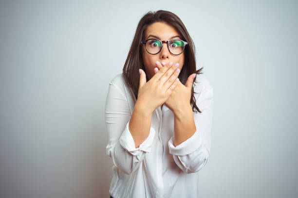 Young beautiful business woman wearing glasses over isolated background shocked covering mouth with hands for mistake. Secret concept. Young beautiful business woman wearing glasses over isolated background shocked covering mouth with hands for mistake. Secret concept. oops stock pictures, royalty-free photos & images