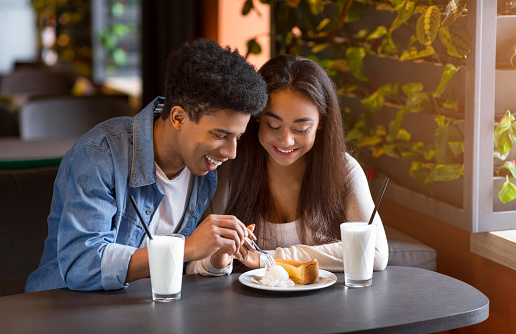 Couple of mixed race teenagers eating cheesecake with ice cream at cafe and smiling, empty space