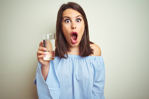 Young beautiful woman drinking a glass of fresh water over isolated background scared in shock with a surprise face, afraid and excited with fear expression