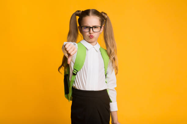 istock Discontented Schoolgirl Gesturing Thumbs Down Over Yellow Background 1174447672