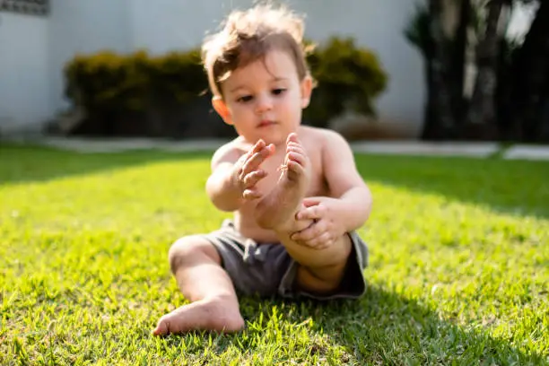 Baby boy playing with feet and grass at sunset