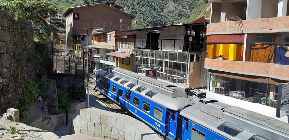 View Of Train Departing, Building Exterior, Andes Mountain, People Walking Around, Sitting Down And More At Aguas Calientes City In Cusco Peru South America