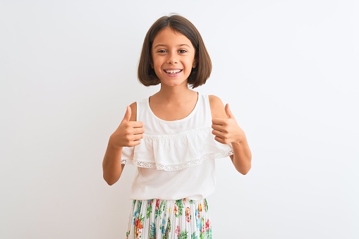 Young beautiful child girl wearing casual dress standing over isolated white background success sign doing positive gesture with hand, thumbs up smiling and happy. Cheerful expression and winner gesture.