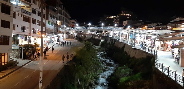 Scene Of Building Exterior, Bridge, Retail Store, Restaurant, People Standing, Walking Around And More In The Night At Aguas Calientes City Center In Cusco Peru South America