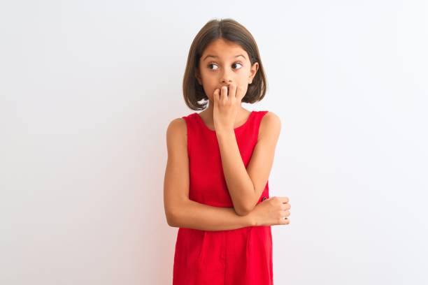 young beautiful child girl wearing red casual dress standing over isolated white background looking stressed and nervous with hands on mouth biting nails. anxiety problem. - nail biting imagens e fotografias de stock