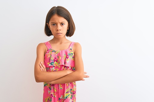 Young beautiful child girl wearing pink floral dress standing over isolated white background skeptic and nervous, disapproving expression on face with crossed arms. Negative person.