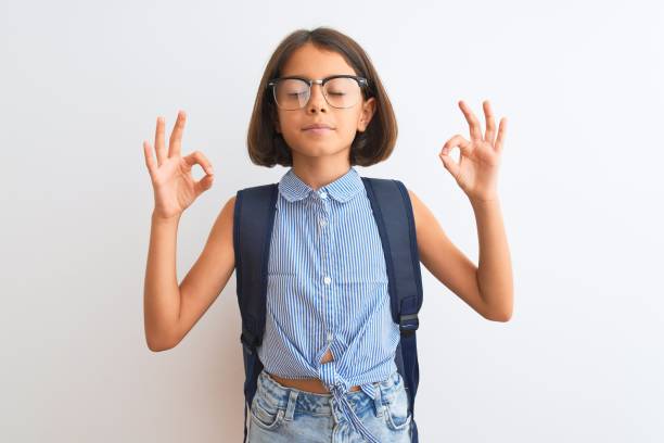 Beautiful student child girl wearing backpack and glasses over isolated white background relax and smiling with eyes closed doing meditation gesture with fingers. Yoga concept. Beautiful student child girl wearing backpack and glasses over isolated white background relax and smiling with eyes closed doing meditation gesture with fingers. Yoga concept. mindfulness children stock pictures, royalty-free photos & images
