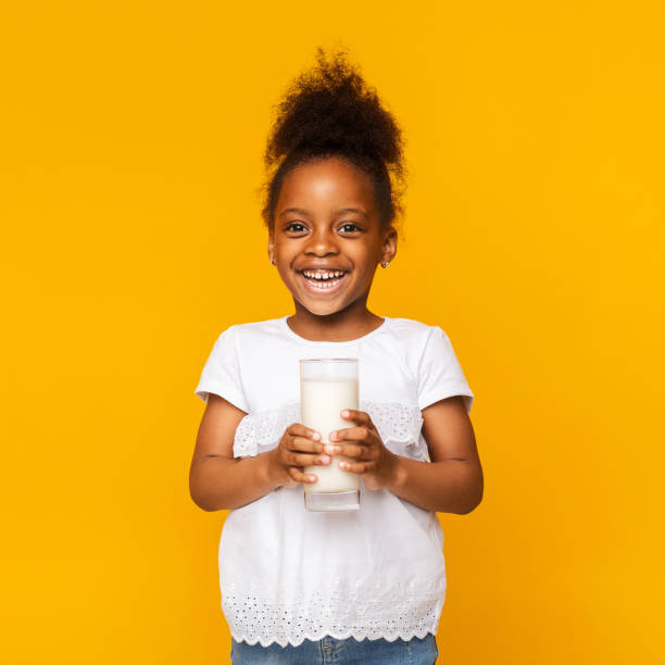 fille afro mignonne appréciant le verre du lait - milk child drinking little girls photos et images de collection