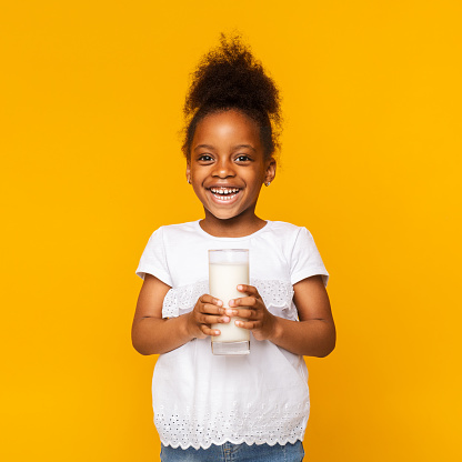 Benefits of dairy products drinking. Cute afro girl enjoying glass of milk, orange studio background