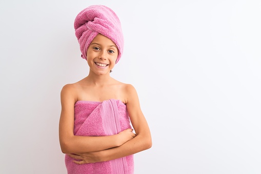 Beautiful child girl wearing shower towel after bath standing over isolated white background happy face smiling with crossed arms looking at the camera. Positive person.