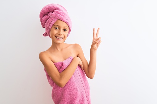 Beautiful child girl wearing shower towel after bath standing over isolated white background smiling with happy face winking at the camera doing victory sign. Number two.