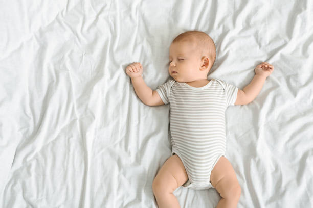 istock Cute infant baby in striped bodysuit sleeping on bed 1174450494