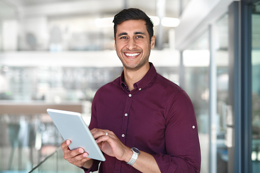 Cropped portrait of a handsome young businessman using a digital tablet while standing in modern office