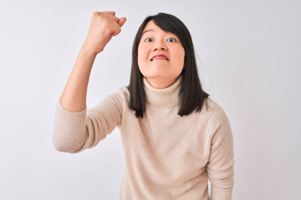 고립 된 흰색 배경에 터틀넥 스웨터를 입은 젊은 아름다운 중국 여성은 분노와 함께 외치면서 좌절하고 분노를 일으키며 주먹을 불끈 쥐었다. 분노와 공격적인 개념. - fist women punching asian ethnicity 뉴스 사진 이미지