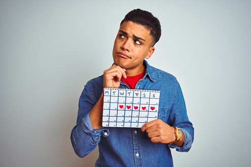 Young brazilian man holding calendar standing over isolated white background serious face thinking about question, very confused idea