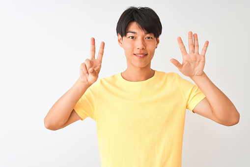 Chinese man wearing yellow casual t-shirt standing over isolated white background showing and pointing up with fingers number seven while smiling confident and happy.