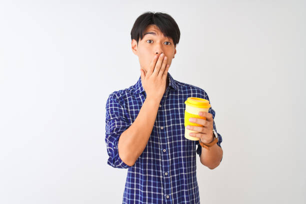 istock Young chinese man drinking take away coffee standing over isolated white background cover mouth with hand shocked with shame for mistake, expression of fear, scared in silence, secret concept 1174459076