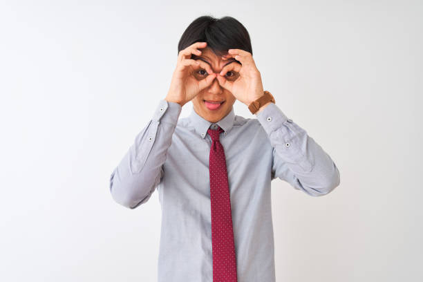 istock Chinese businessman wearing elegant tie standing over isolated white background doing ok gesture like binoculars sticking tongue out, eyes looking through fingers. Crazy expression. 1174459310