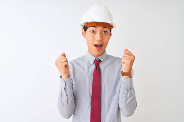 istock Chinese architect man wearing tie and helmet standing over isolated white background celebrating surprised and amazed for success with arms raised and open eyes. Winner concept. 1174459502