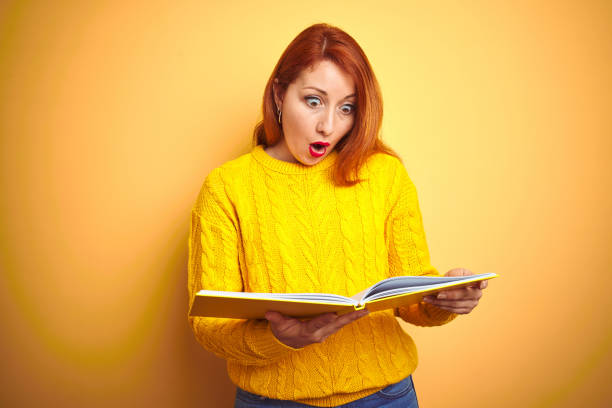 istock Young redhead student woman reading book standing over yellow isolated background scared in shock with a surprise face, afraid and excited with fear expression 1174462994