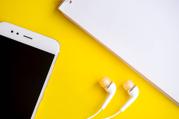 istock White smart phone and headphones with notepad yellow background. 1174466002