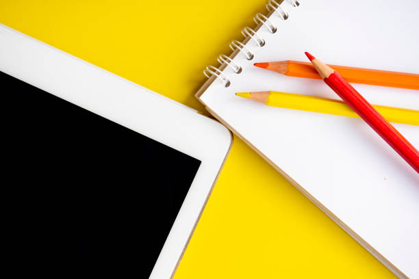 istock Tablet and notepad with color pencils on the yellow background. 1174466006
