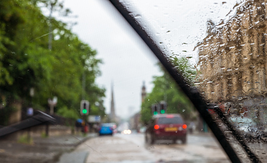 Wet car outside rear view mirror covered with water drops during a rain, inside view in selective focus through the side window