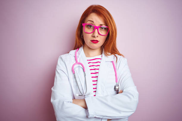 istock Young redhead doctor woman using stethoscope standing over isolated pink background skeptic and nervous, disapproving expression on face with crossed arms. Negative person. 1174466769