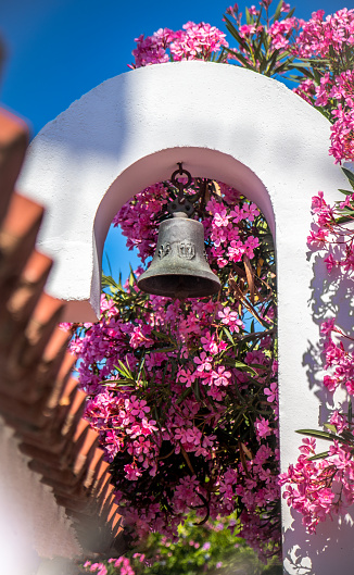 Sunny day on the Greek island with traditional little chapel and white belfry surrounded with pink bougainvilleas flowers.