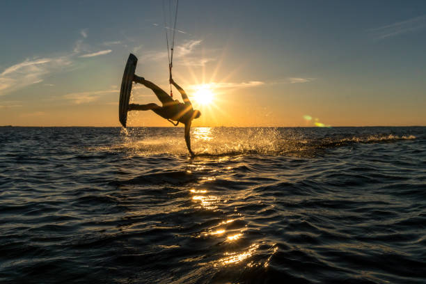 kitesurfer doing handslide in sunset with sunstar and beautiful silhouette kitesurfer doing handslide in sunset with sunstar and beautiful silhouette sonne stock pictures, royalty-free photos & images
