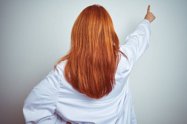 istock Young redhead doctor woman using stethoscope over white isolated background Posing backwards pointing ahead with finger hand 1174467423