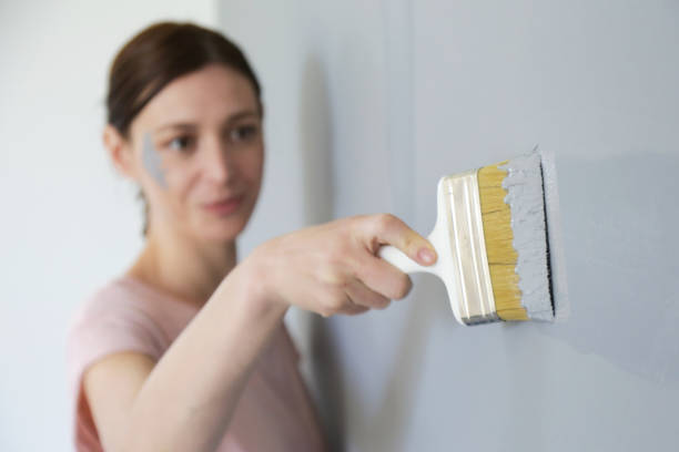 istock Woman painting with gray paint over a white wall 1174468744