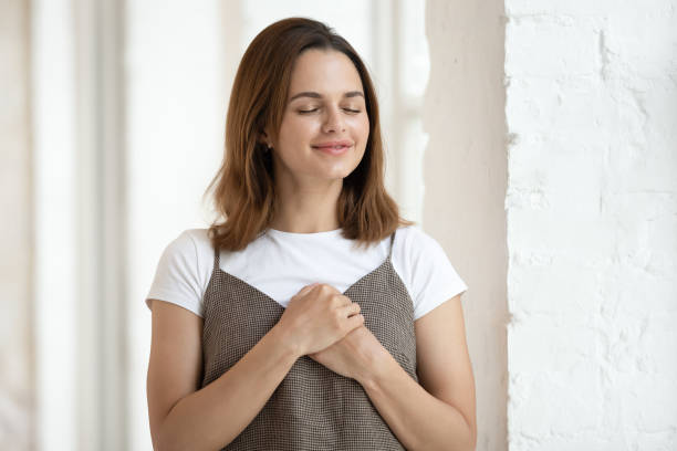 frau halten beide handflächen auf der brust drücken dankbarkeit aus - spirituality hand on heart meditating women stock-fotos und bilder