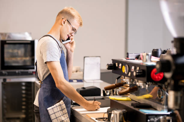 istock Young waiter or worker of cafeteria writing down orders of clients in notepad 1174473284