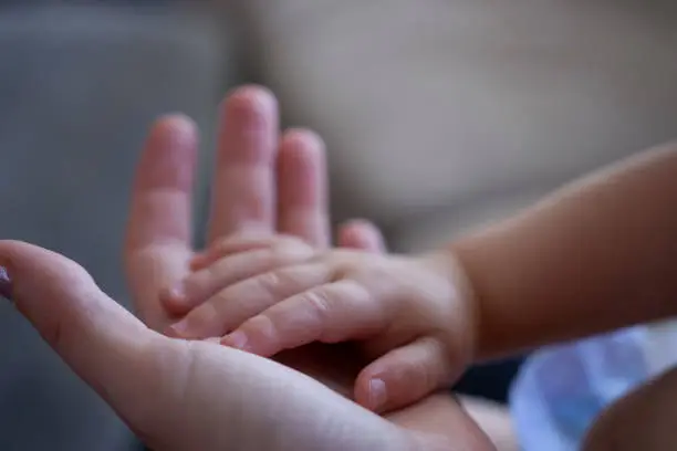 a Mother holds her babies hand in hers with shallow focus and natural lighting