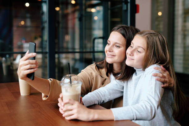 istock Affectionate mother and daughter with drinks looking at smartphone camera 1174478059