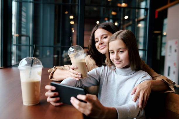 istock Happy mother embracing her daughter with smartphone while both watching video 1174478109