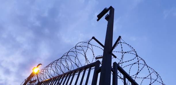 istock Barbed wire fence and lighting at night. Security fence. 1174479596