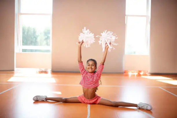 Photo of Dark-skinned little cheerleader doing leg split while practicing