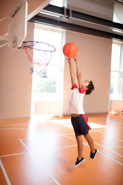 Photo of Schoolboy wearing sport clothing throwing ball into basket