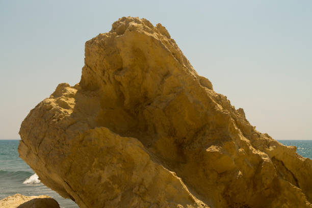 Part of a big rough yellow sea cliff in sunlight in front of the blue sky