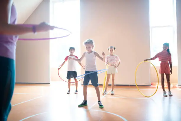 Photo of Boys and girls rolling hula-hoops at physical training