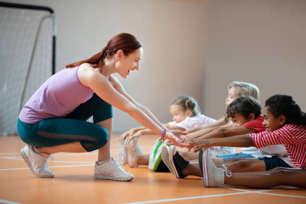 professeur de pe utilisant des leggings souriant tout en aidant l'étirement de fille - éducation physique photos et images de collection