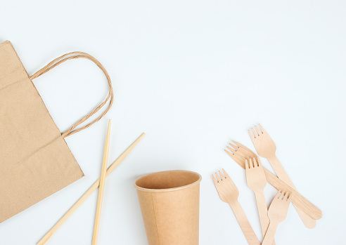 Disposable tablewar of natural materials. Eco friendly concept. Wooden forks, empty craft coffee cup, bag, chopsticks on a white background. Copy space. Top view