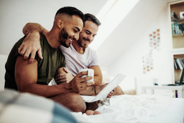Gay couple at home using internet and laptop to chat with friends Gay couple at home in penthouse man gay stock pictures, royalty-free photos & images