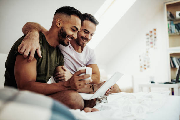 gay couple at home using internet and laptop to chat with friends - couple home interior laptop computer imagens e fotografias de stock