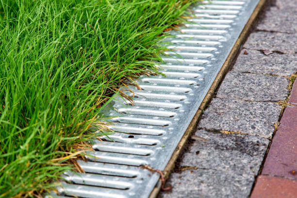 istock An iron gutter with grate to the drainage system on the side of the footpath paved with stone tiles and green lawn, close up. 1174487125